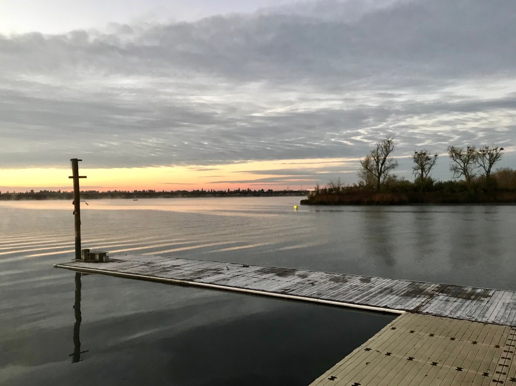An icy dock surrounded by calm water on a cloudy morning right before sunrise.
