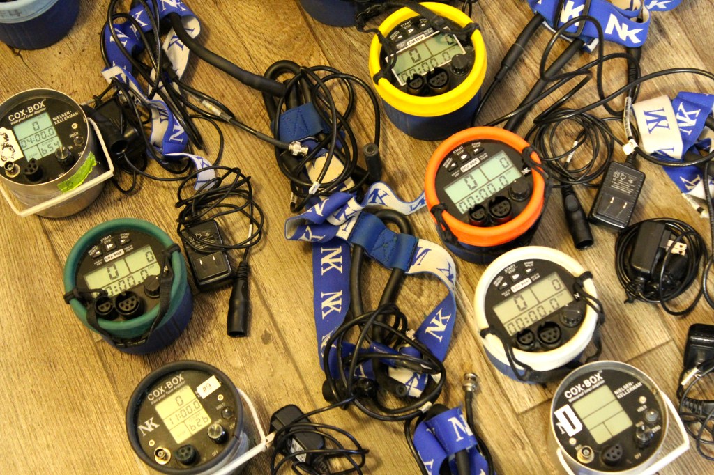 Cox boxes that are turned on, their headsets, and chargers in two organized lines.