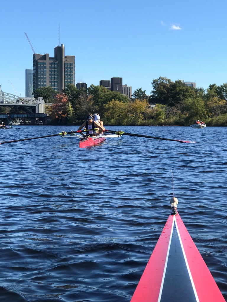 A rower stretching in a rowing shell on the water.