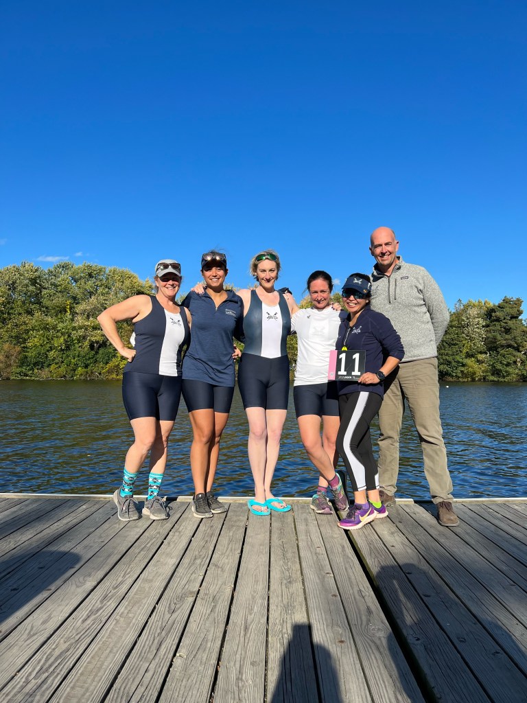 Four rowers, a coxswain and a coach standing at a dock.